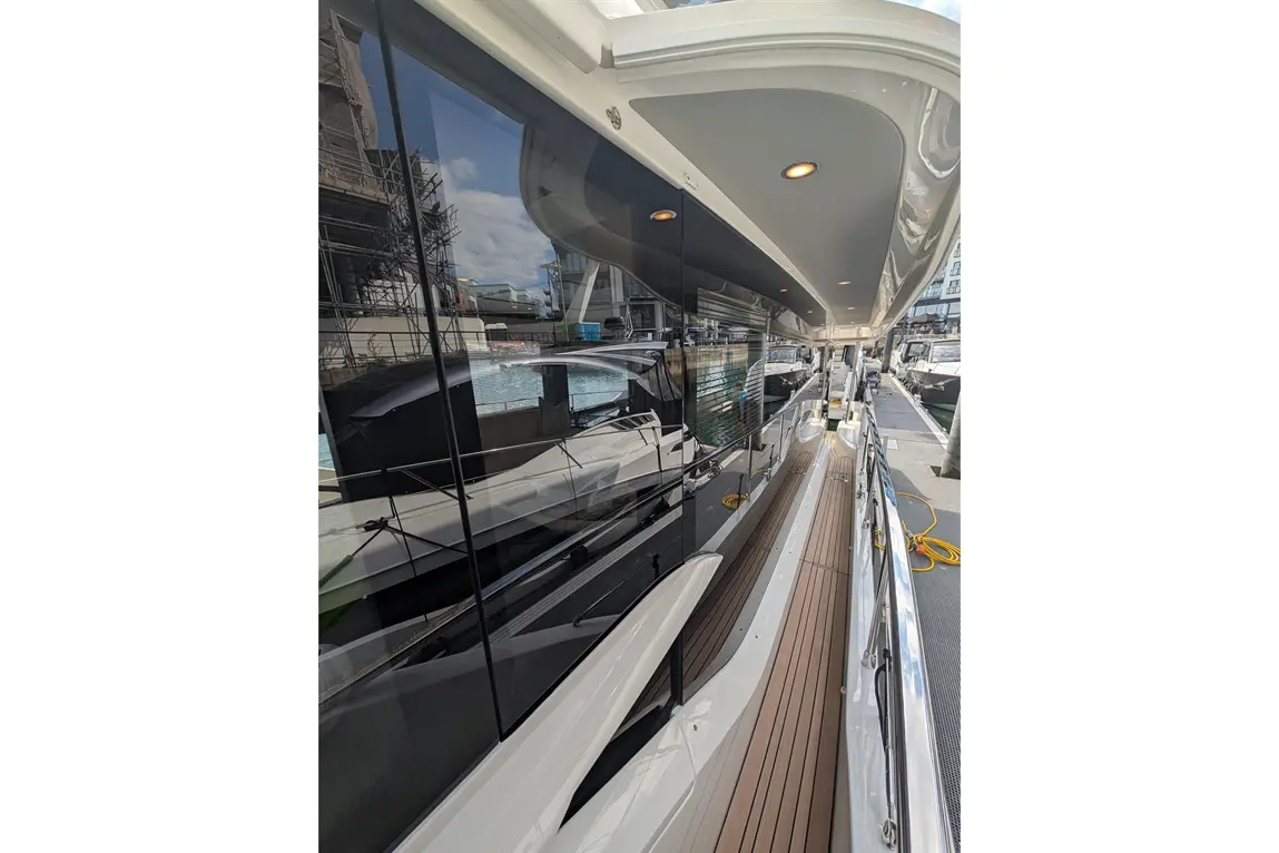 Luxury yacht deck with polished surfaces, reflecting surroundings; docked at marina with boats and construction in background.